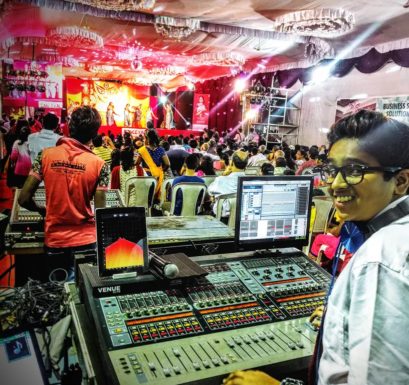 At a live sound and lighting desk, a lit stage behind