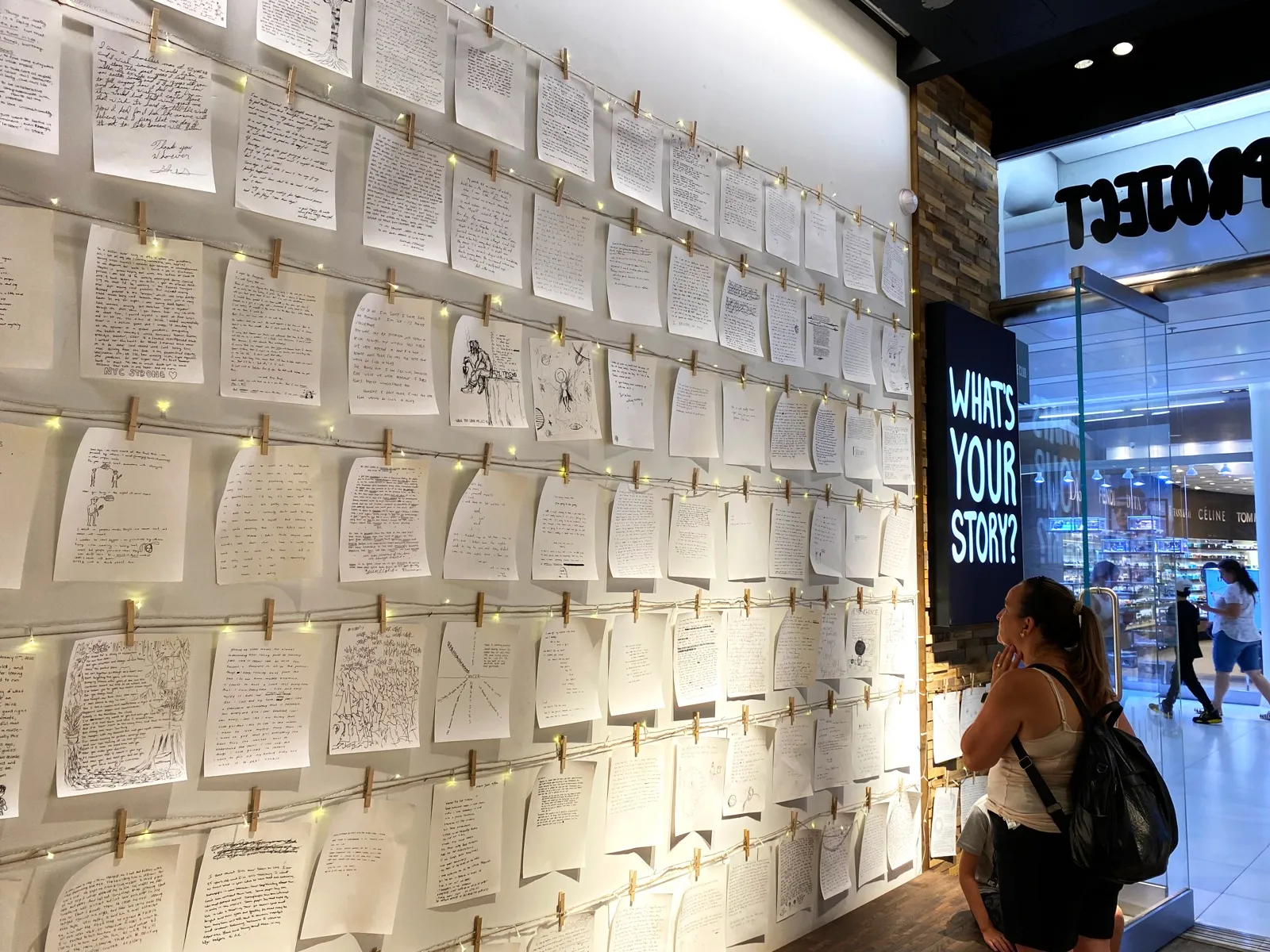 A wall of handwritten pages pegged on strings, a woman reading them